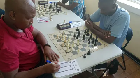 Two players at a tournament board, one recording the moves on a score sheet
